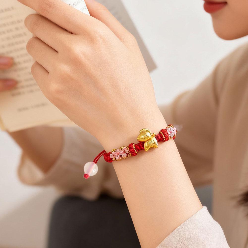 Vòng tay nữ phong cách dân tộc với thiết kế bện thủ công, nút dây đỏ và họa tiết hoa đào.