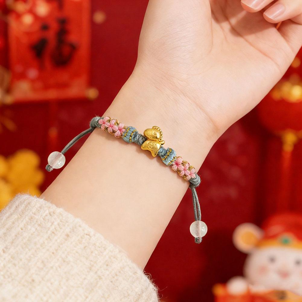 Vòng tay nữ phong cách dân tộc với thiết kế bện thủ công, nút dây đỏ và họa tiết hoa đào.