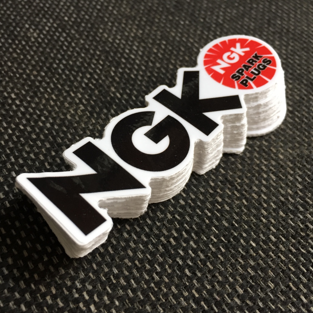 NGK[8.5X2.4cm] decal cao cấp chống nước, sắc nét, bền màu, dính chặt. Hình dán logo trang trí mọi nơi, in theo yêu cầu